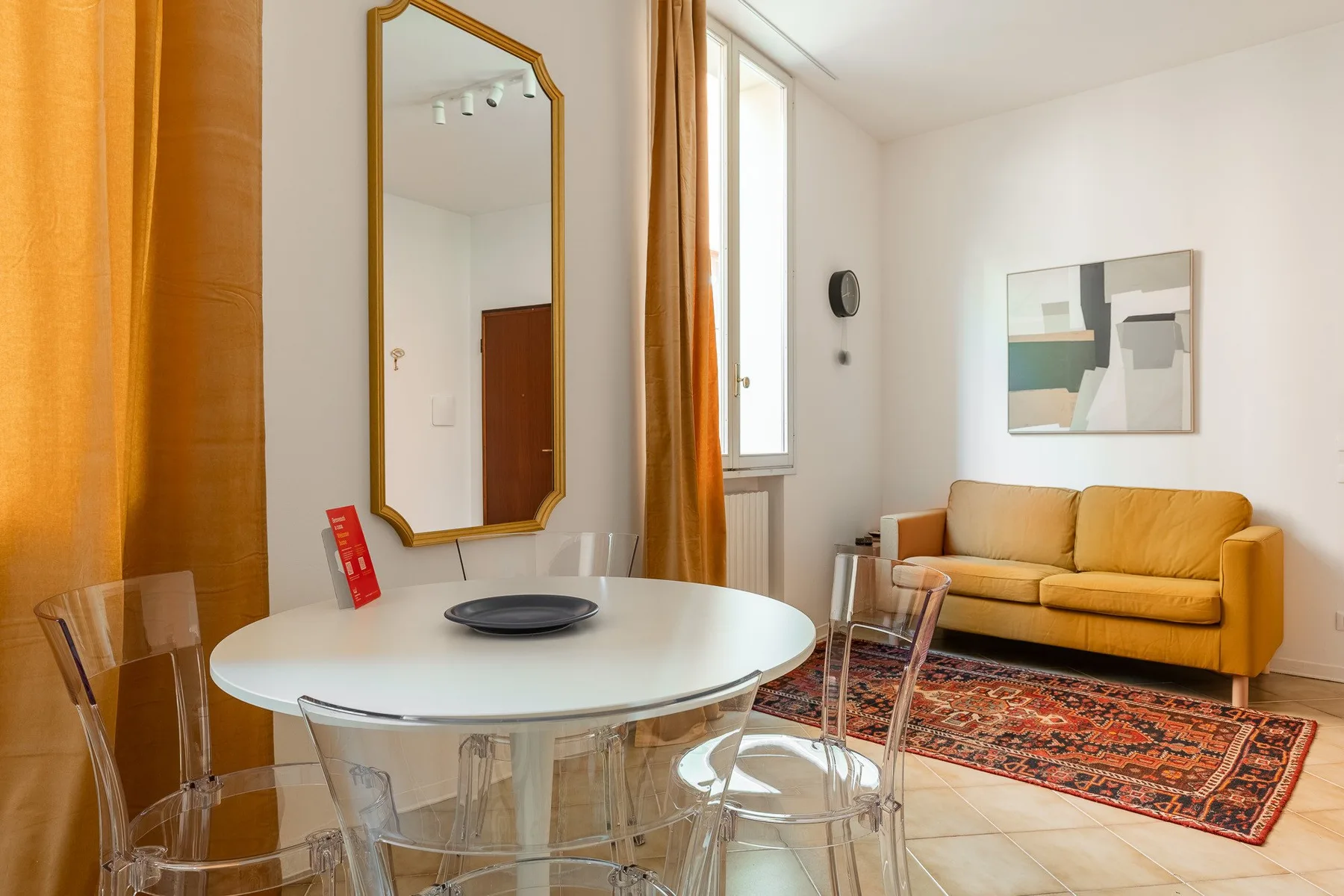 Una luminosa sala de estar y comedor con una mesa redonda, asientos transparentes y un sofá amarillo.