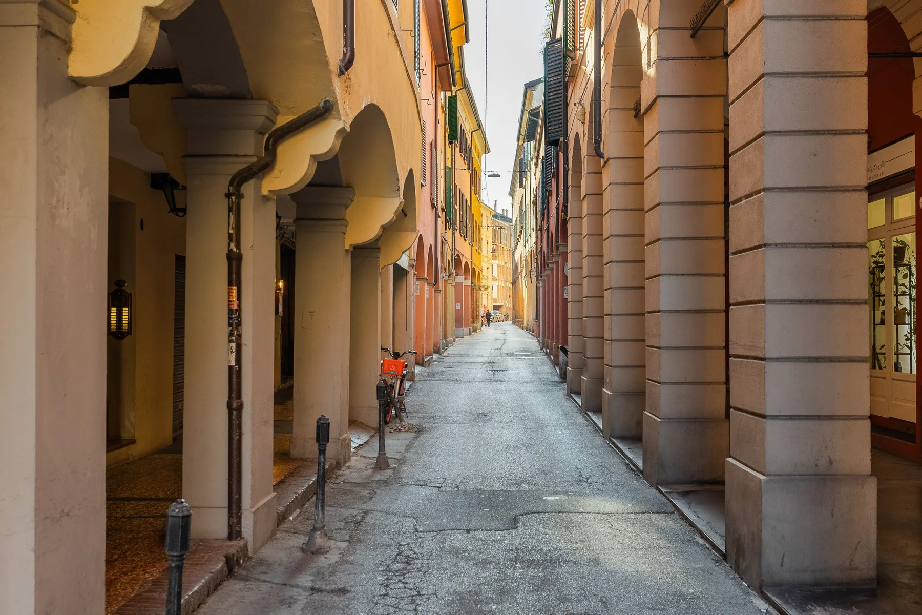 Una calle urbana estrecha flanqueada por edificios y arcadas cubiertas.
