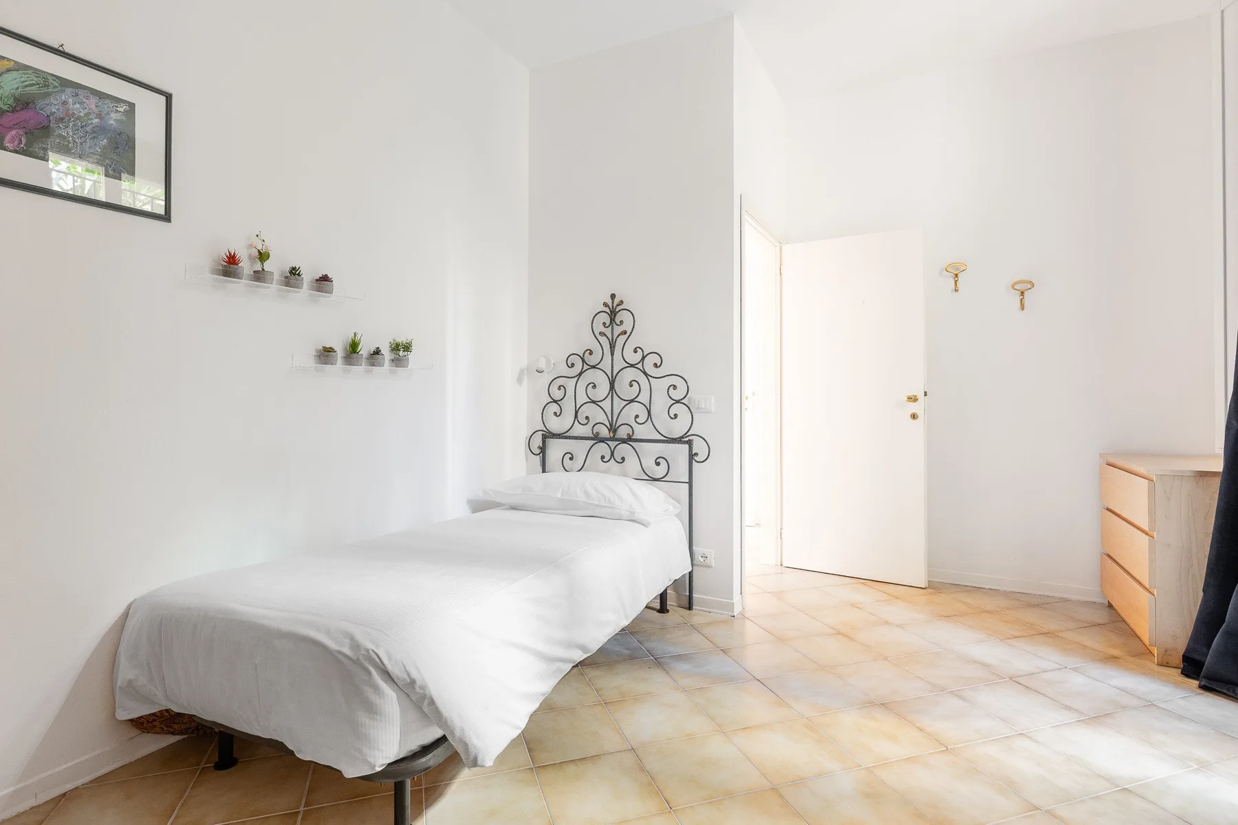 Un dormitorio luminoso con una cama blanca y un cabecero decorativo de metal.