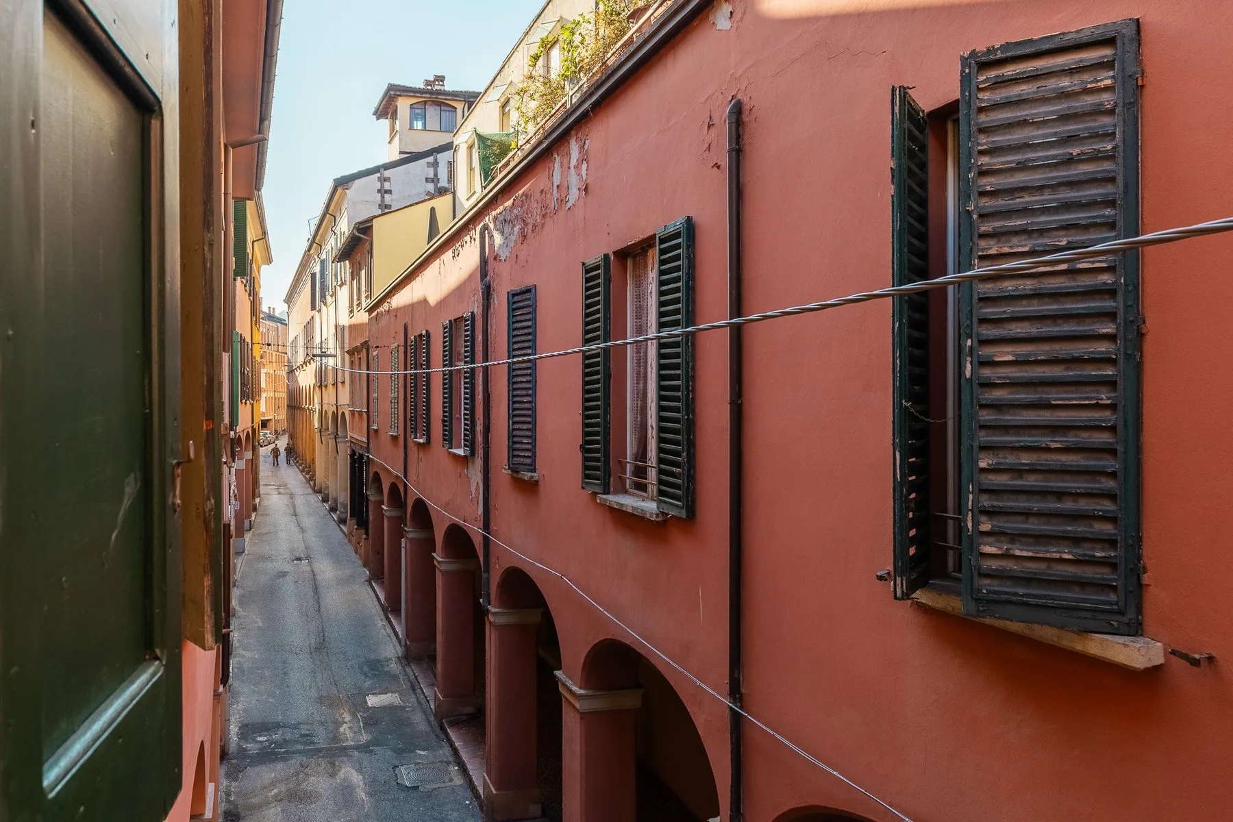 Un callejón estrecho pavimentado pasa junto a un largo edificio rojo con contraventanas oscuras.