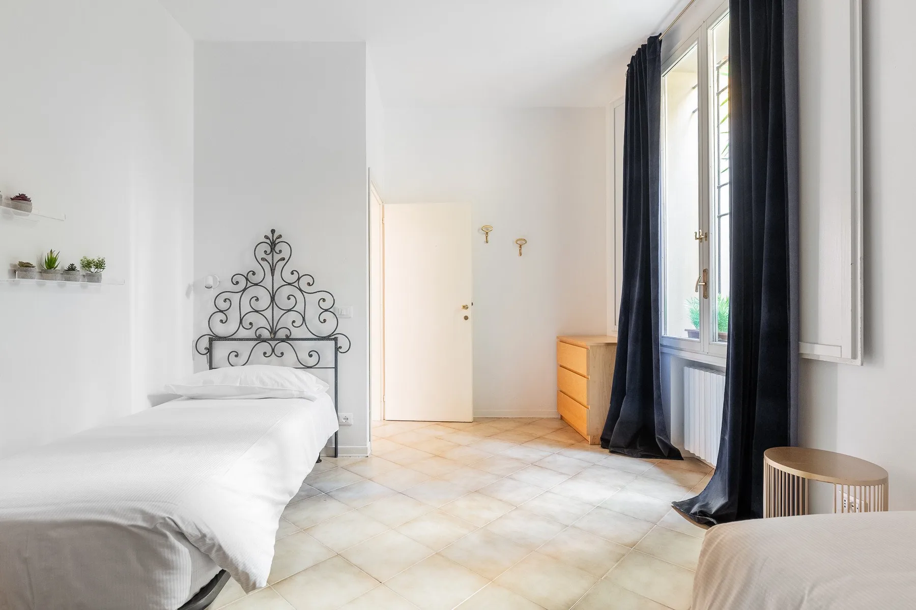 Un dormitorio luminoso con una cama de hierro forjado y ventanas altas con cortinas oscuras.