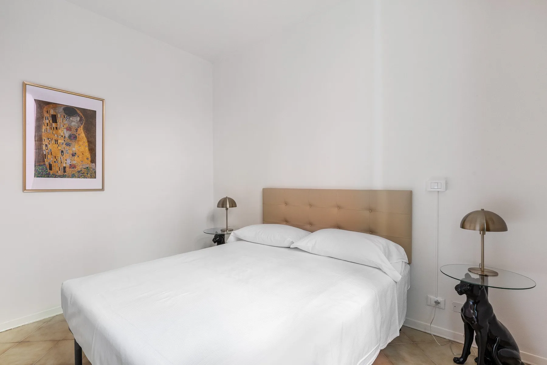 Un dormitorio luminoso con una cama bien tendida y una obra enmarcada en la pared.