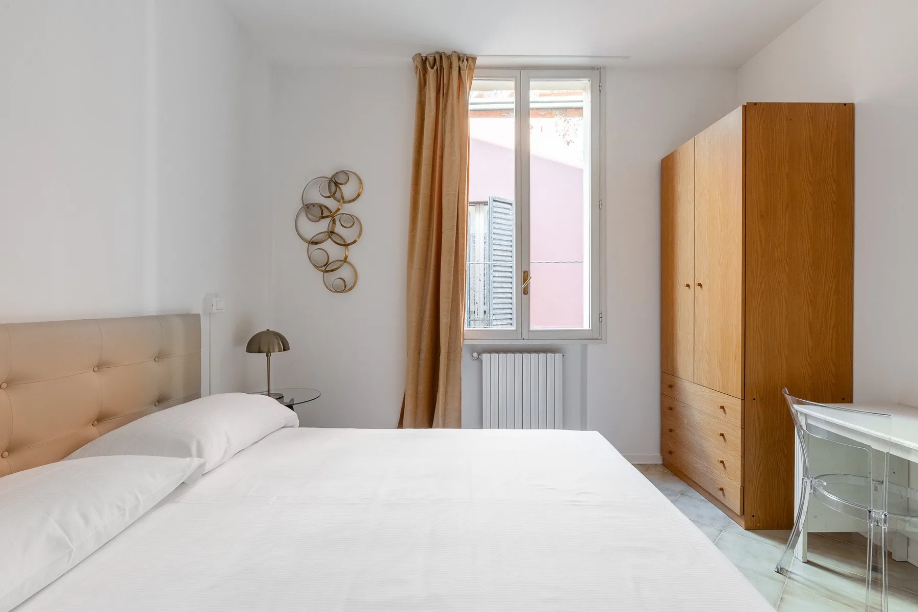 Un dormitorio luminoso con cama, armario de madera y ventana.