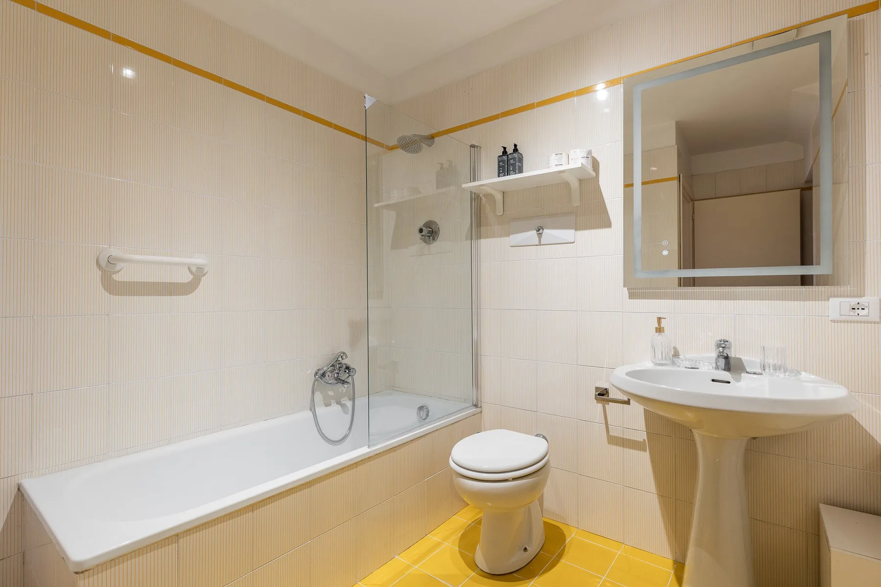 Un baño alicatado con bañera, inodoro y lavabo bajo un espejo.