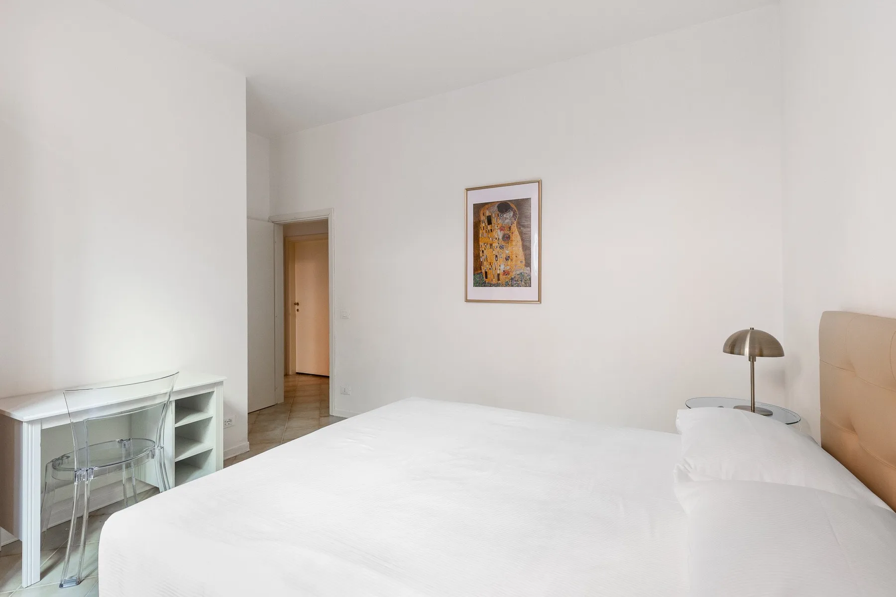 Un dormitorio luminoso con una cama grande, un escritorio pequeño y arte enmarcado en la pared.