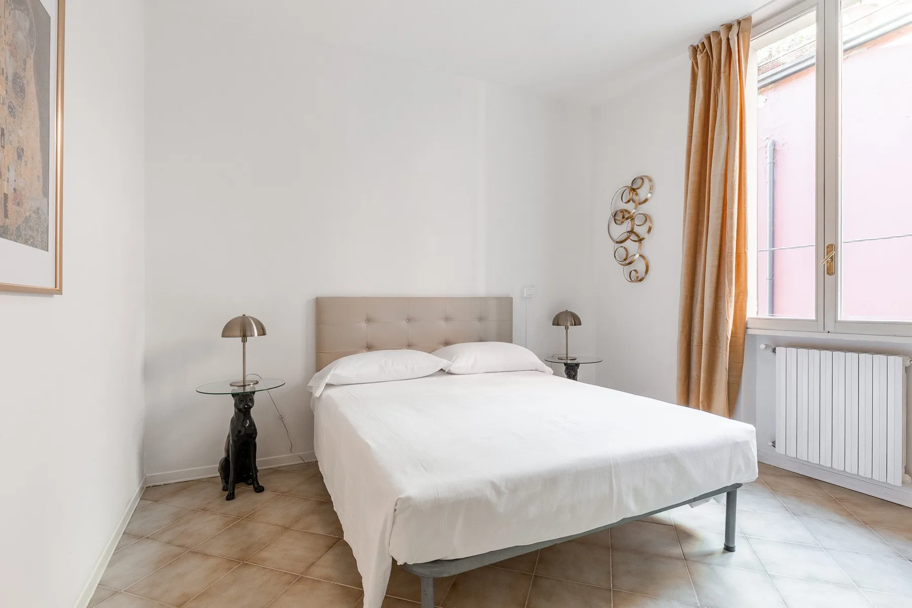 Un dormitorio luminoso con una cama bien tendida y una ventana grande.