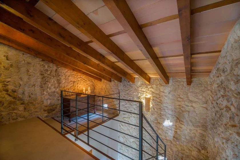 Un interior de paredes de piedra con vigas de madera expuestas y una barandilla metálica.