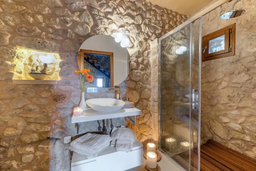 Un baño con paredes de piedra, lavabo, espejo y ducha de vidrio.