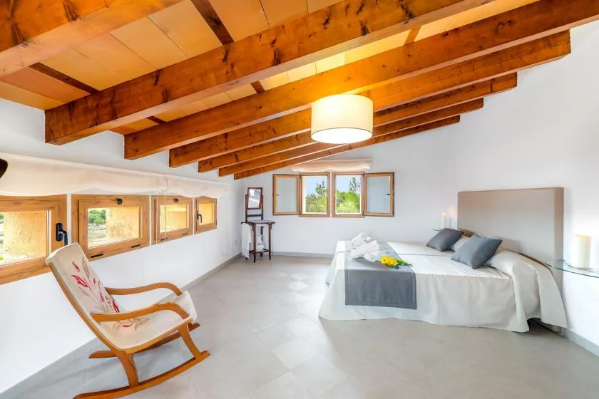 Un dormitorio luminoso con una cama, una mecedora y vigas de madera a la vista.