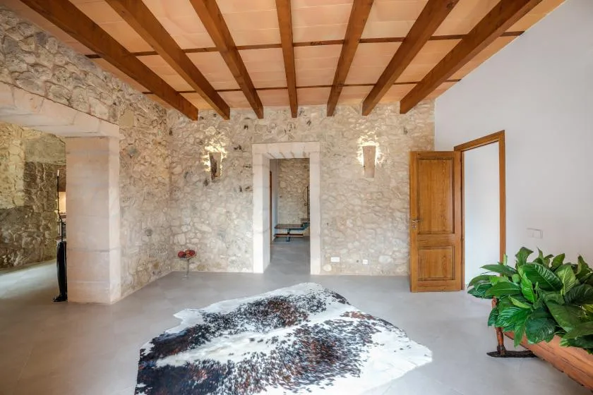 Una habitación con paredes de piedra, vigas de madera a la vista y una alfombra estampada.