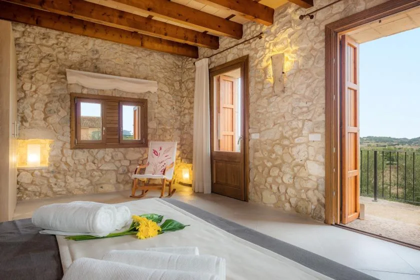 Un dormitorio de piedra rústica con una cama de madera y puertas abiertas a un balcón.