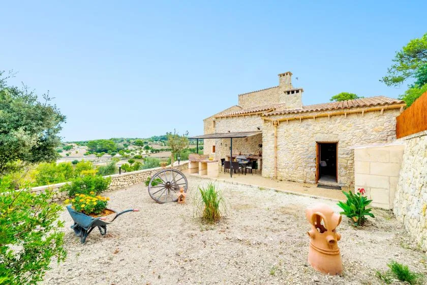 Una casa de piedra da a un patio de grava con asientos al aire libre y plantas.