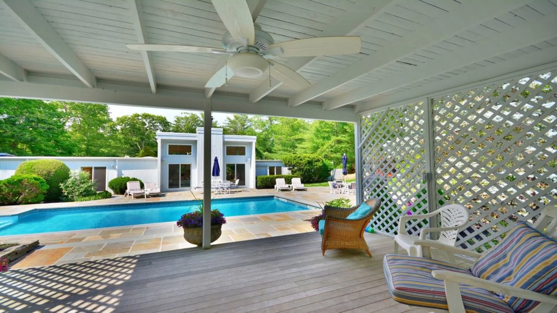 A covered patio overlooks a swimming pool, with seating beneath a ceiling fan.