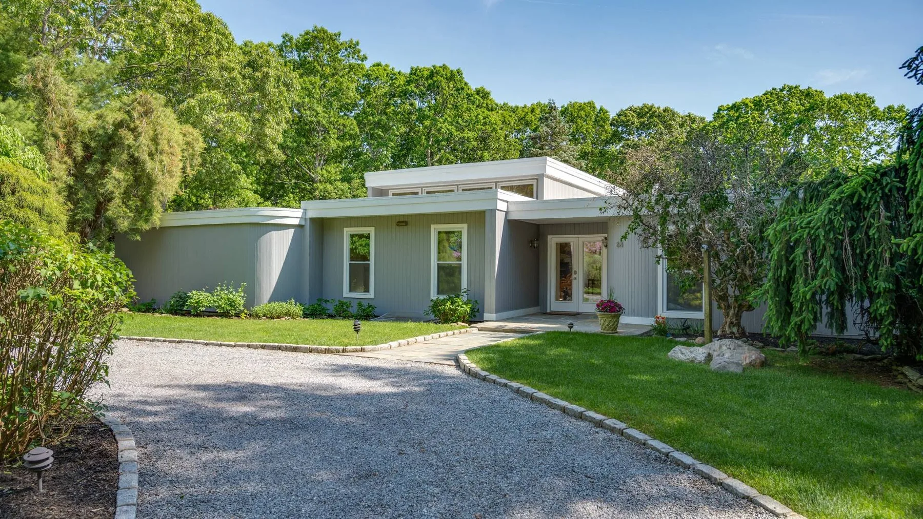 A modern single-story house faces a curved gravel driveway and landscaped lawn.