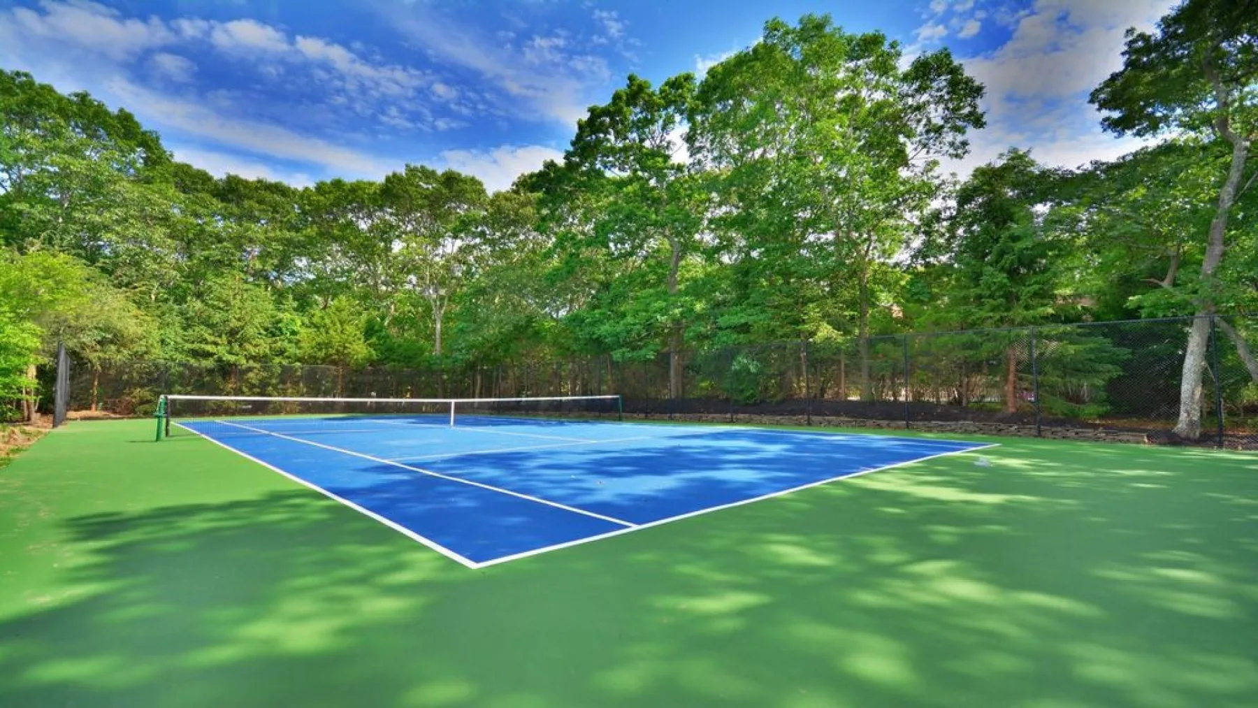 Una pista de tenis azul está rodeada de árboles y una zona verde.
