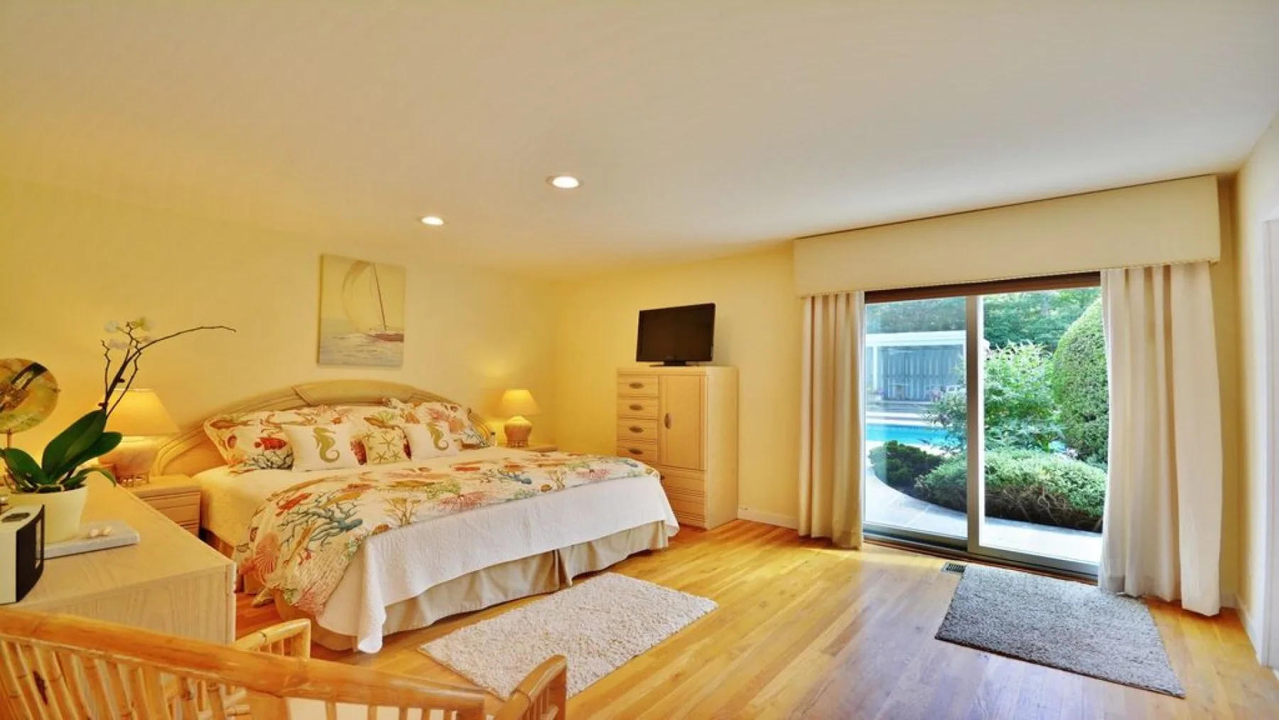 A bright bedroom with a floral bedspread and sliding glass doors opening to a patio.