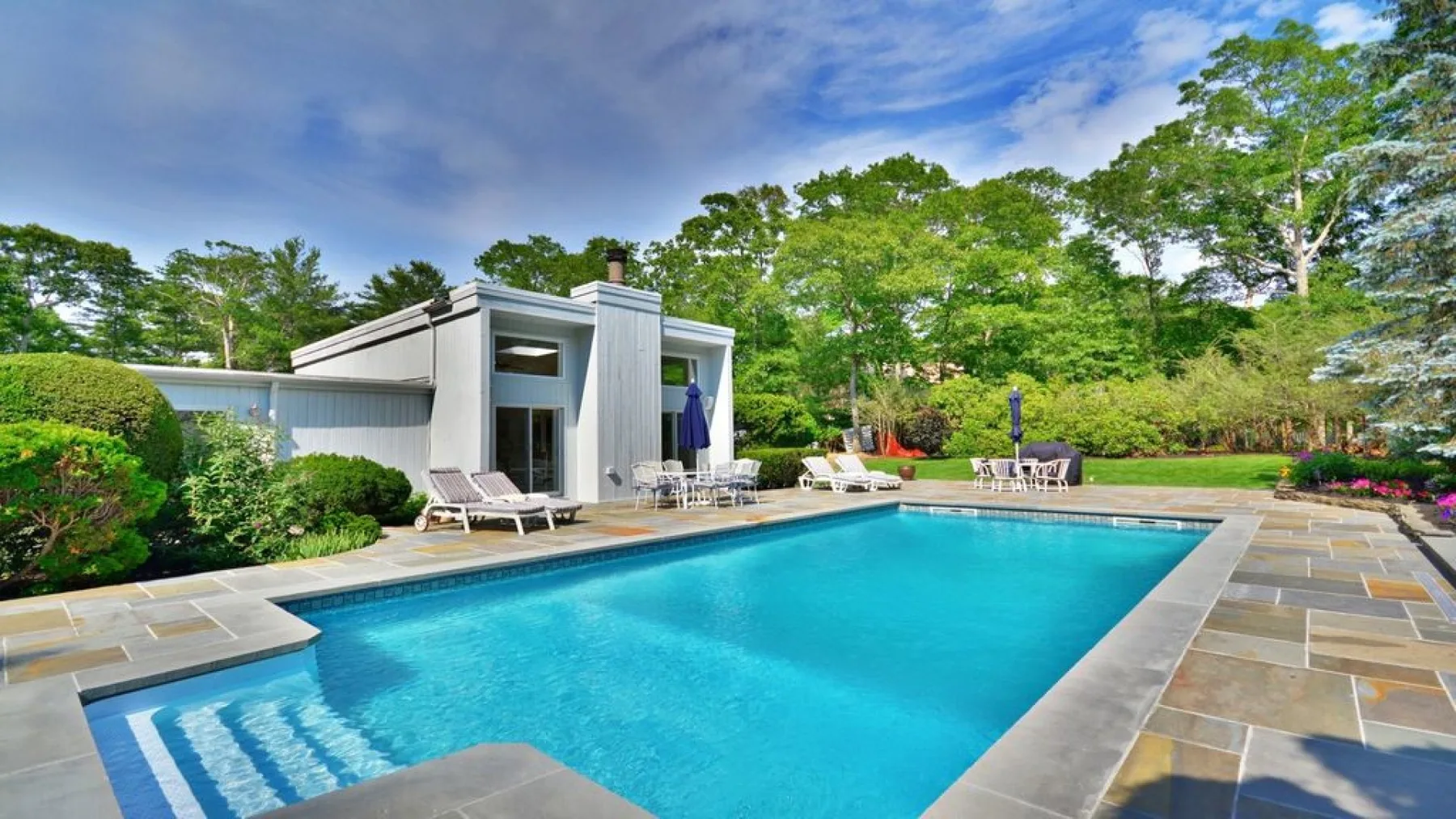 An outdoor swimming pool beside a modern house and landscaped garden.