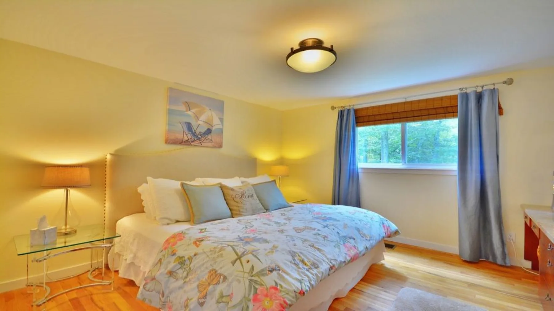 A bedroom with a bed dressed in a floral cover and a window with curtains.