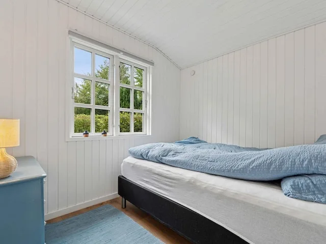 A bright bedroom with a bed and a large window overlooking greenery.