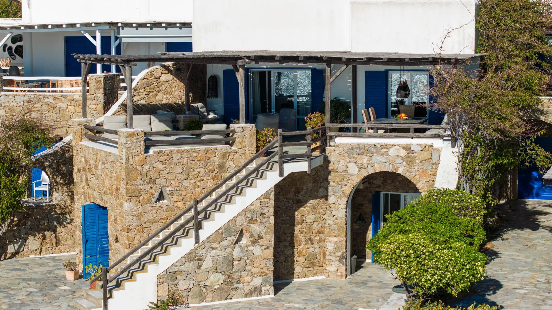 A stone building has an exterior staircase leading to a shaded terrace.