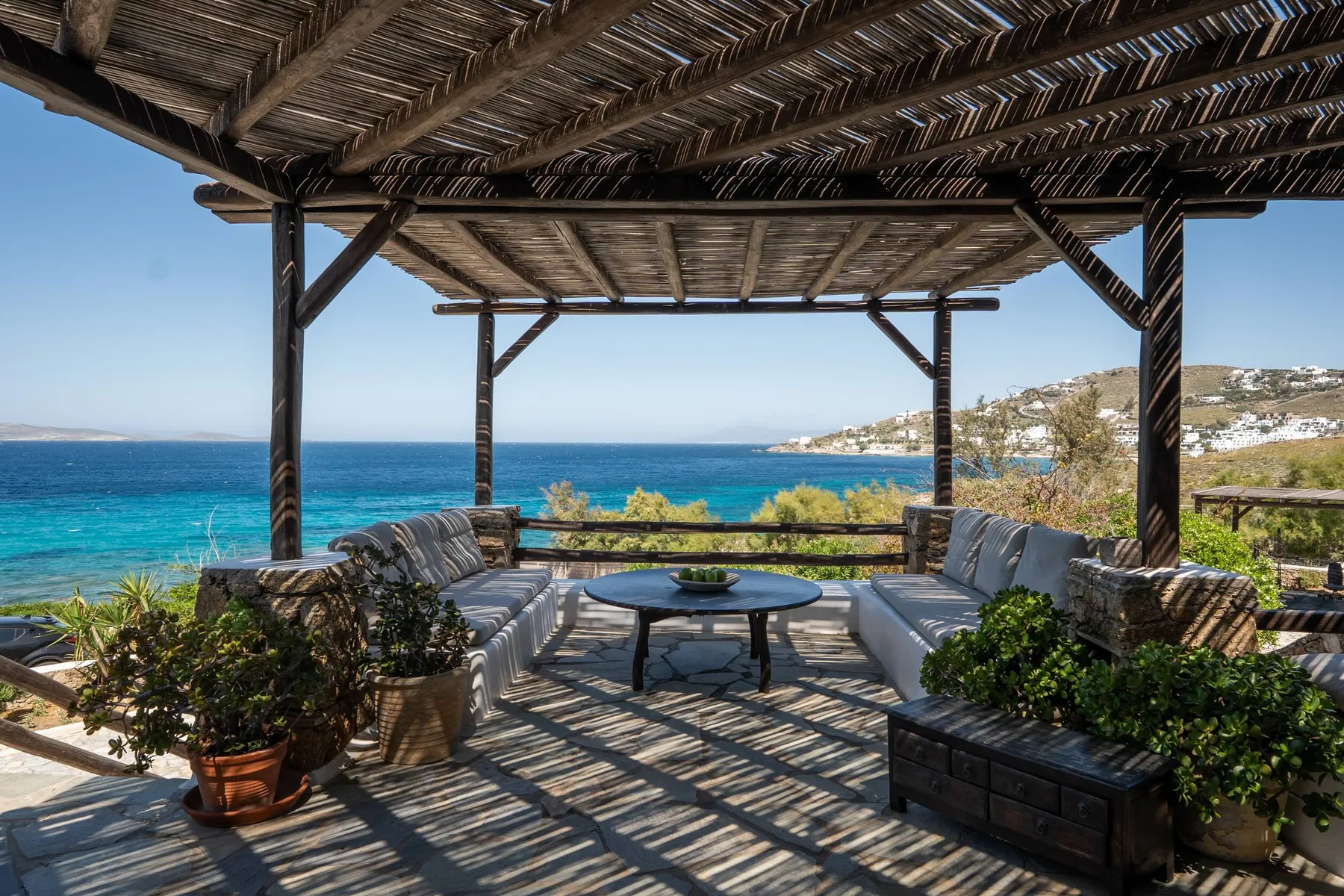 A shaded outdoor seating area overlooks the blue sea.