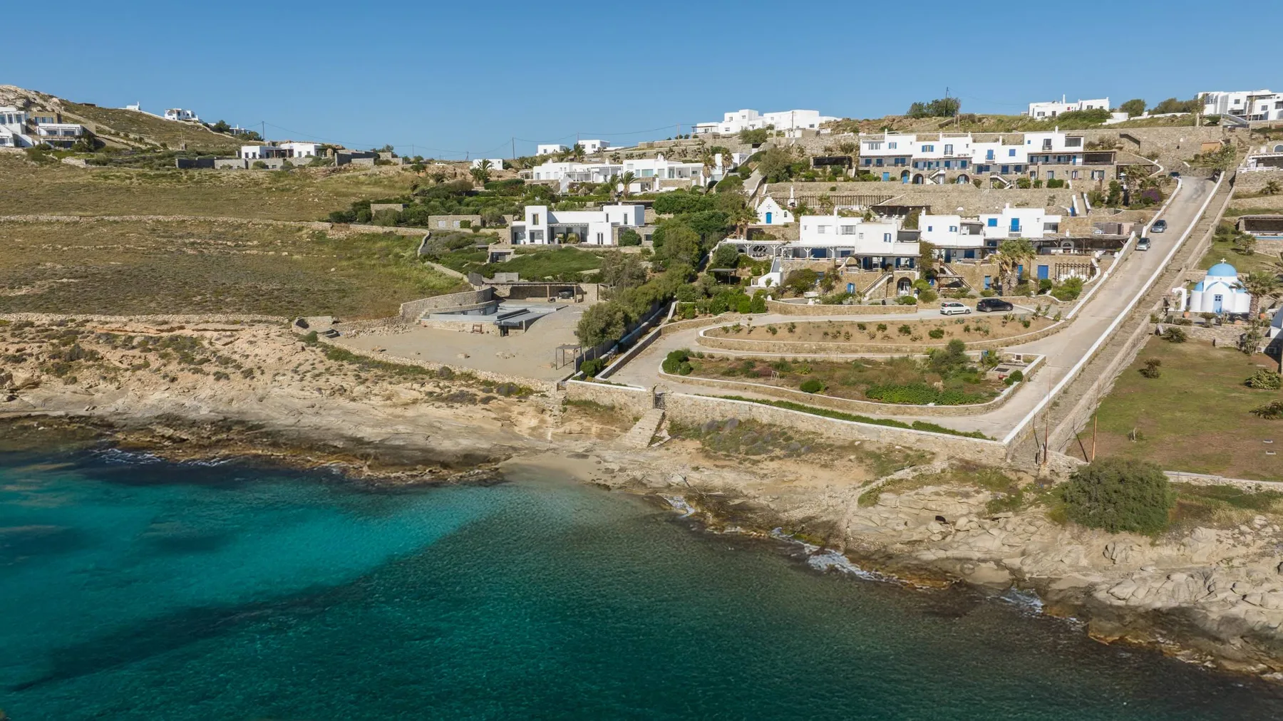 A coastal settlement overlooks rocky shoreline and clear turquoise water.