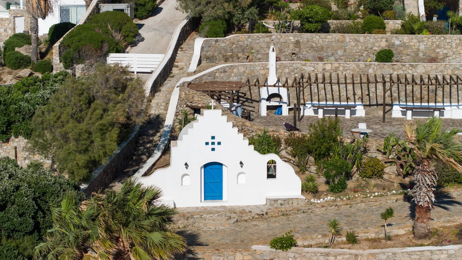 A white stepped-gable building stands below a terrace with a pergola and seating.