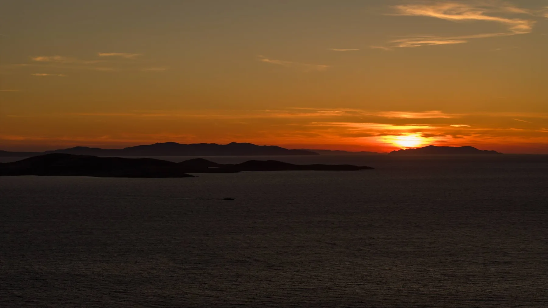 Sunset over the sea, with dark islands silhouetted on the horizon.