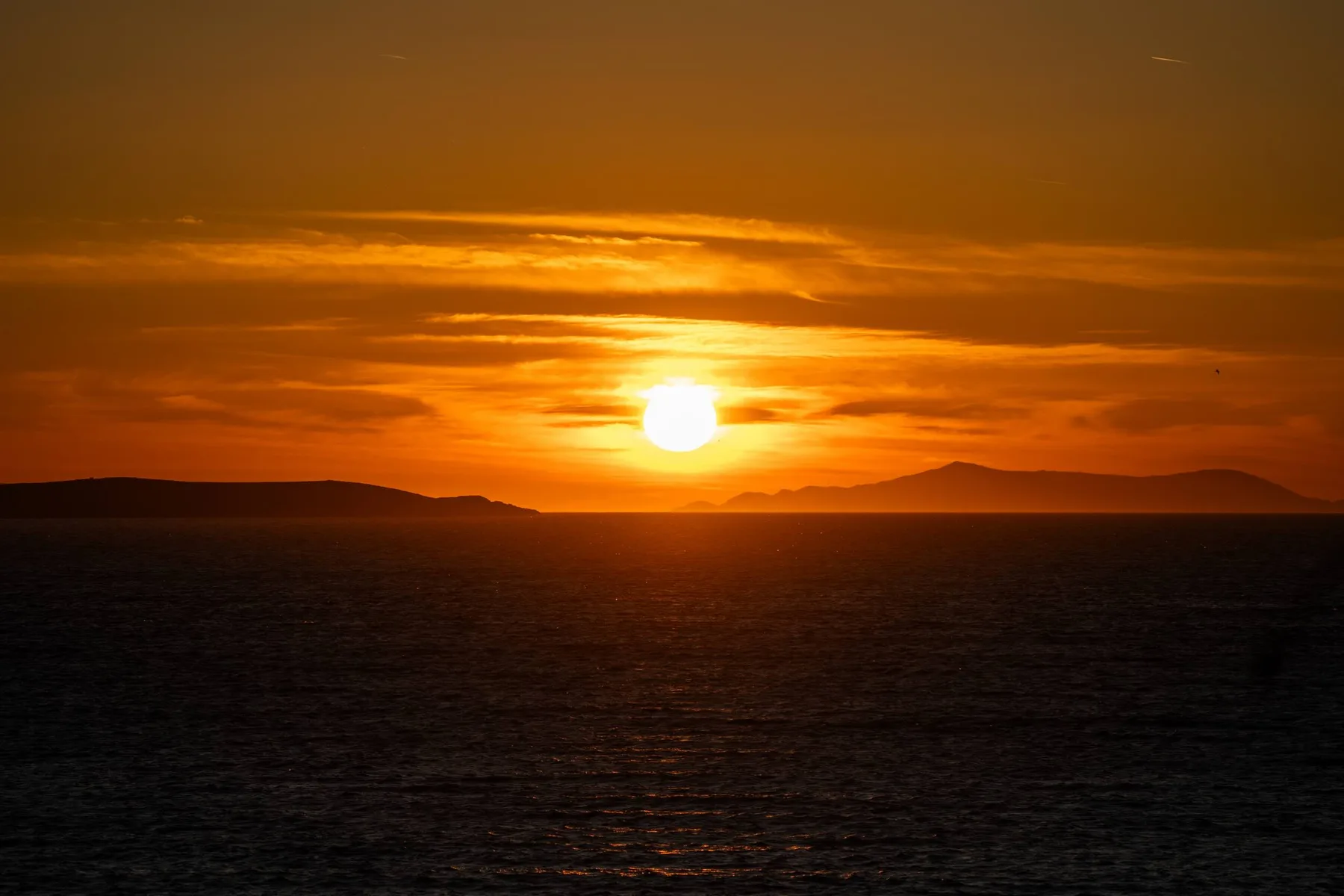 The sun sets over the sea beneath an orange sky.