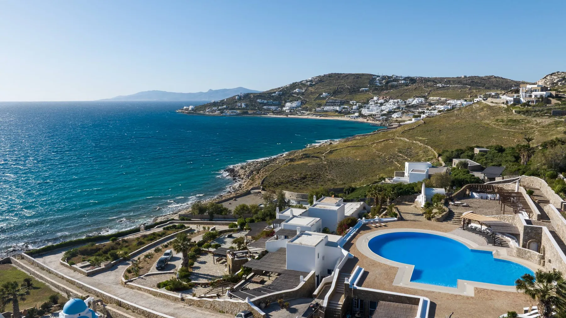 A coastal hillside property overlooks the sea, with a swimming pool in the foreground.