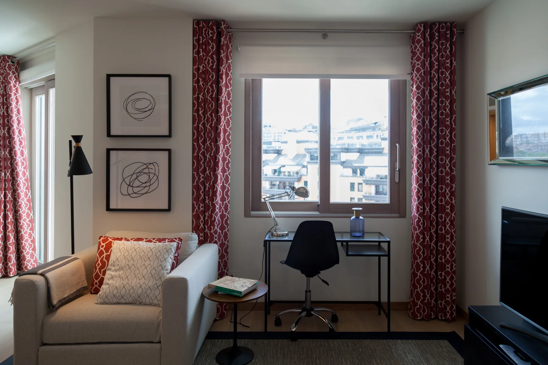 Una sala de estar con escritorio y asientos junto a una ventana grande.