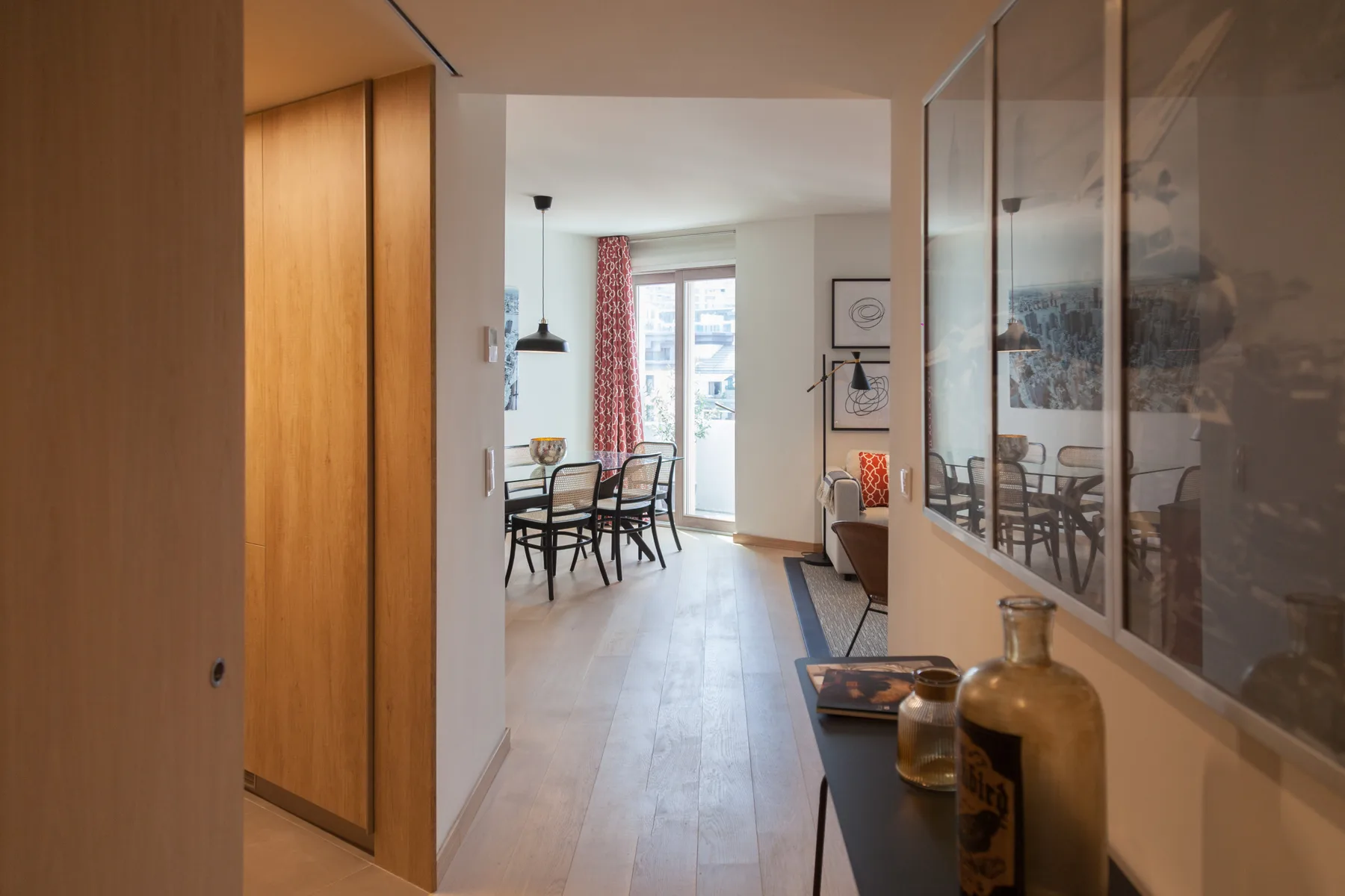 Interior luminoso de un apartamento con comedor y zona de estar junto a grandes ventanas.