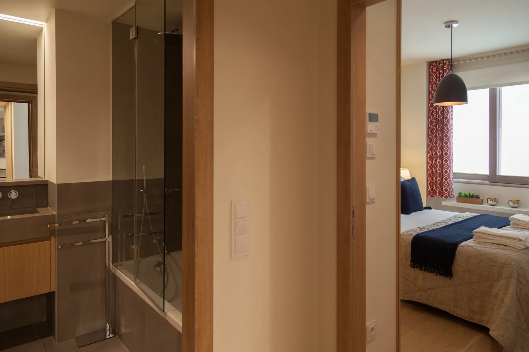 Un baño se abre a un dormitorio con una cama junto a una ventana.