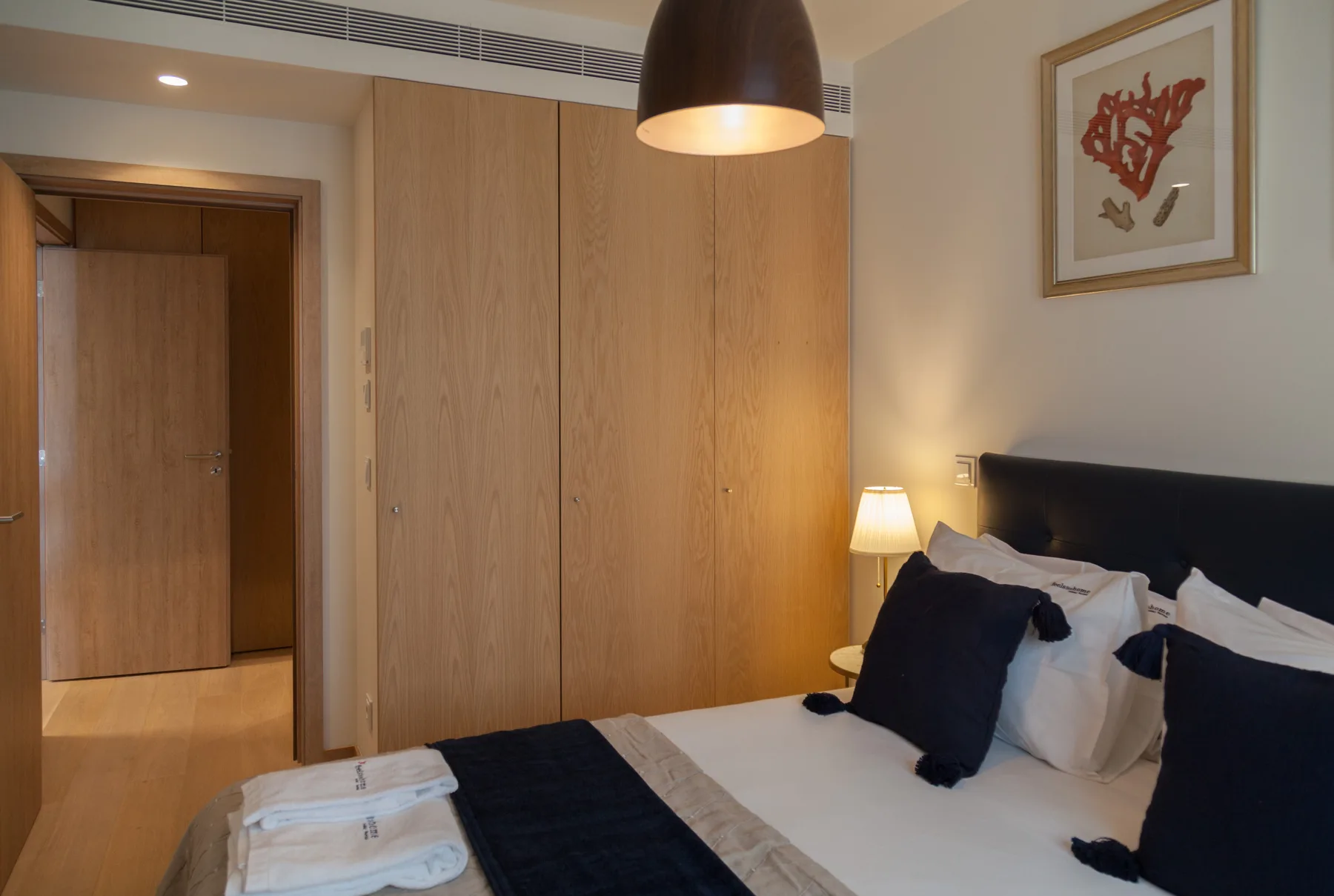 Dormitorio con cama, lámpara de mesilla y armario de madera.