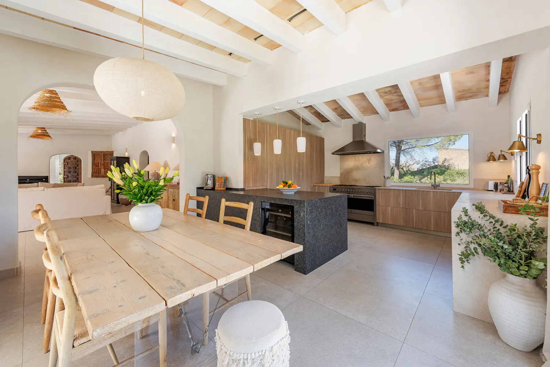 Bright, modern kitchen with wooden table, pendant lights, and light wood cabinetry. Greenery and flowers add a fresh touch.