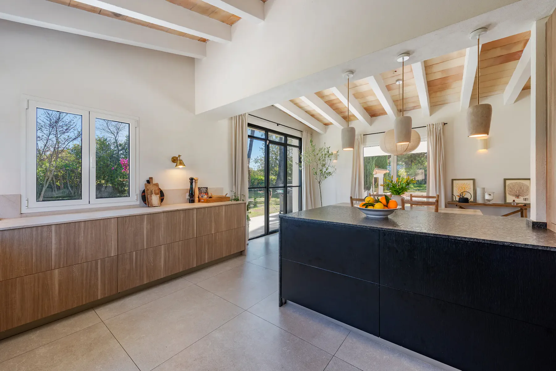 A bright kitchen with a dark island, wooden cabinetry, and pendant lights.