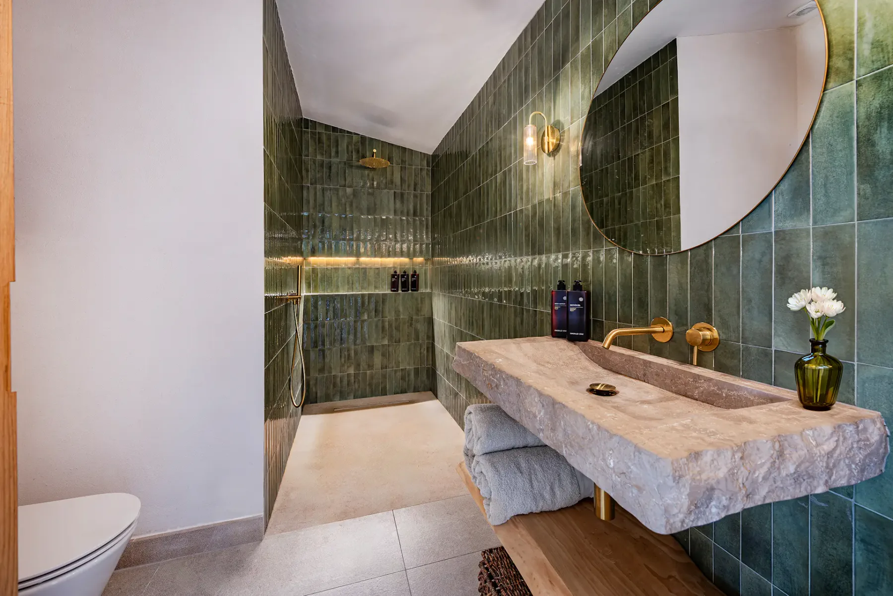 A bathroom with green tiled walls, a stone sink, and a round mirror.