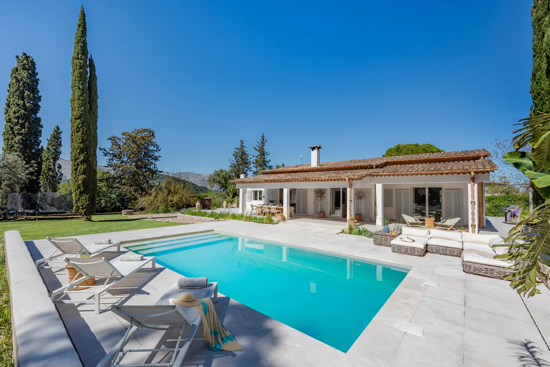 Outdoor pool with lounge seating beside a single-story house under a clear blue sky.