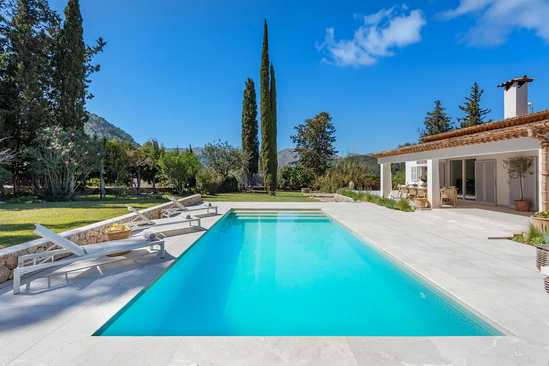 Outdoor swimming pool with lounge chairs beside a house and landscaped grounds.