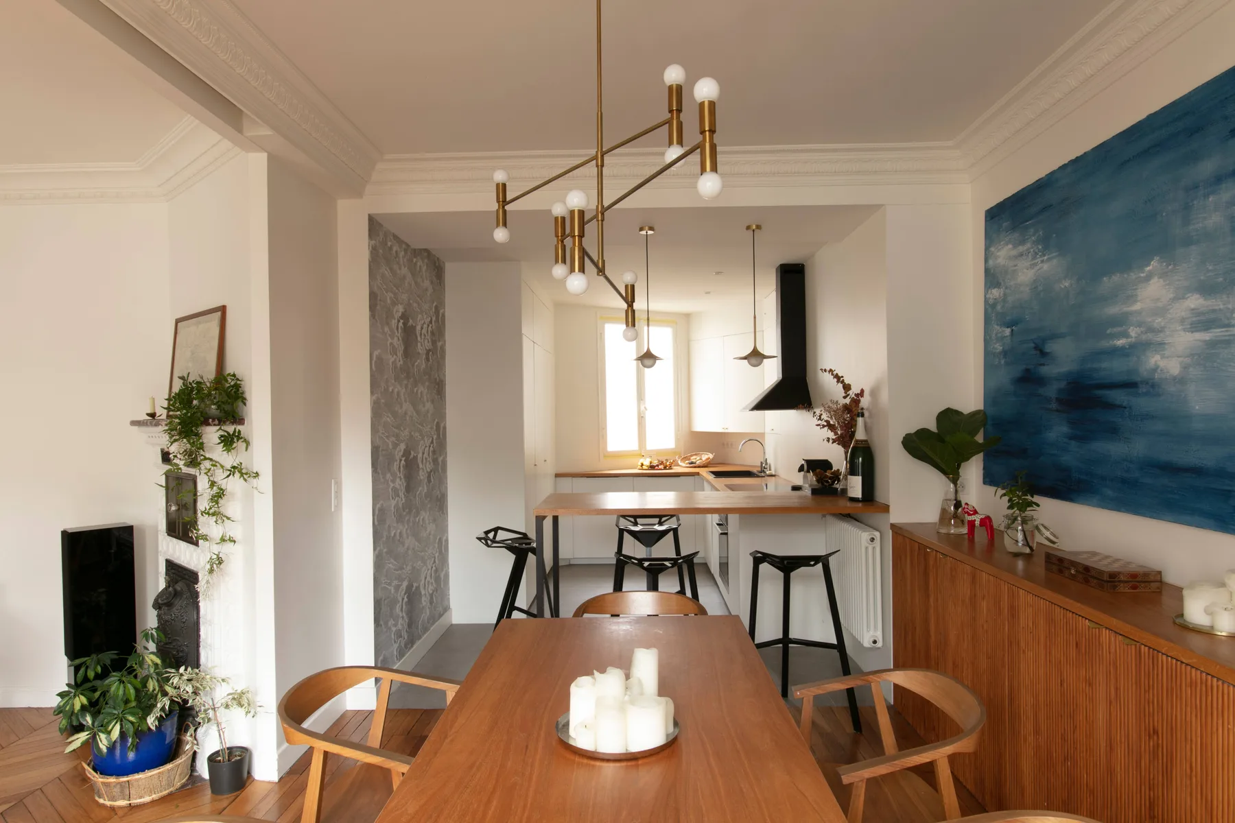 A dining area with a long wooden table, open kitchen, and blue wall art.