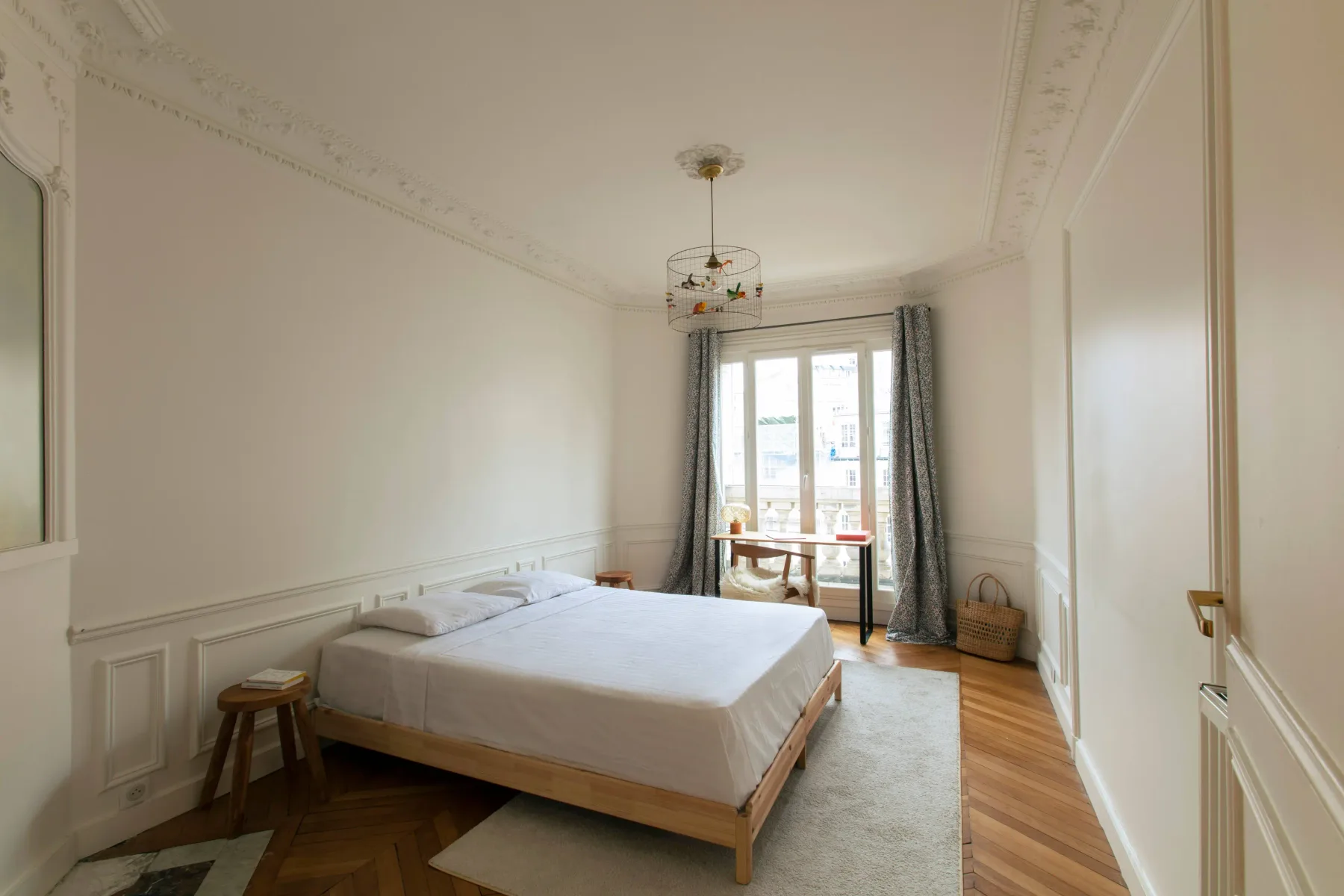 A bright bedroom with a bed beside tall windows and curtains.