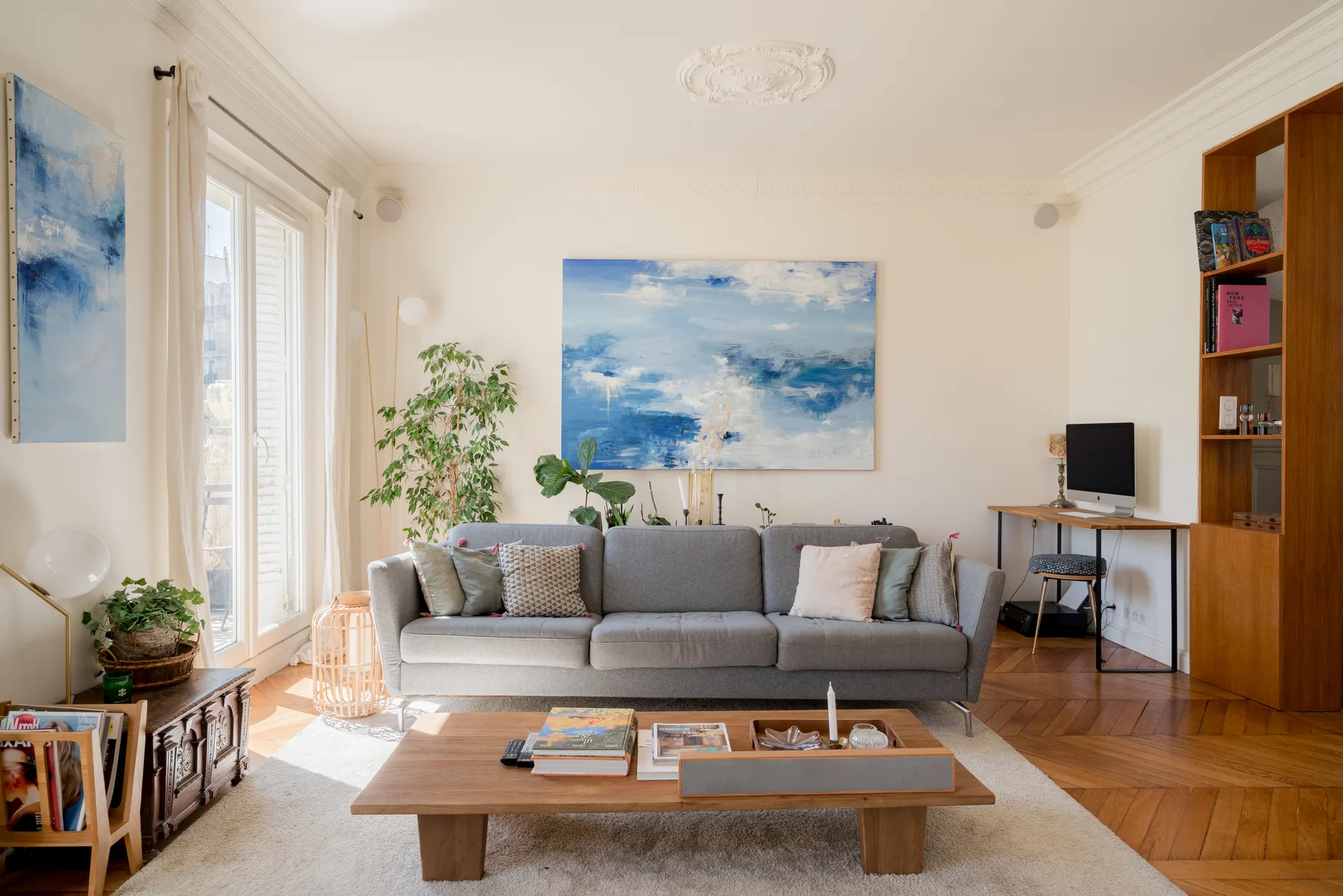 A bright living room with gray seating, abstract artwork, and a low wooden table.