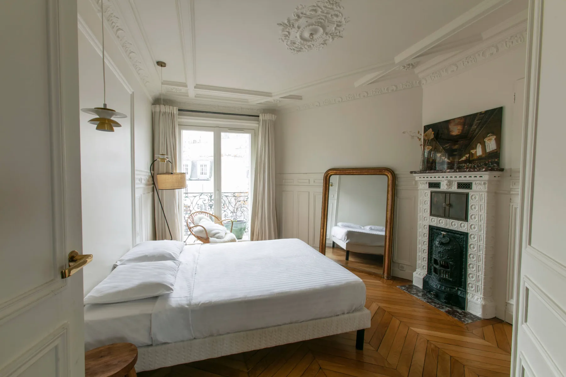 A bright bedroom with a bed, tall mirror, and decorative fireplace.