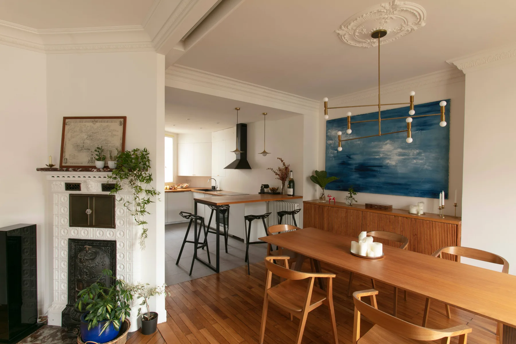A dining area with a long wooden table beside an open kitchen and blue wall art.
