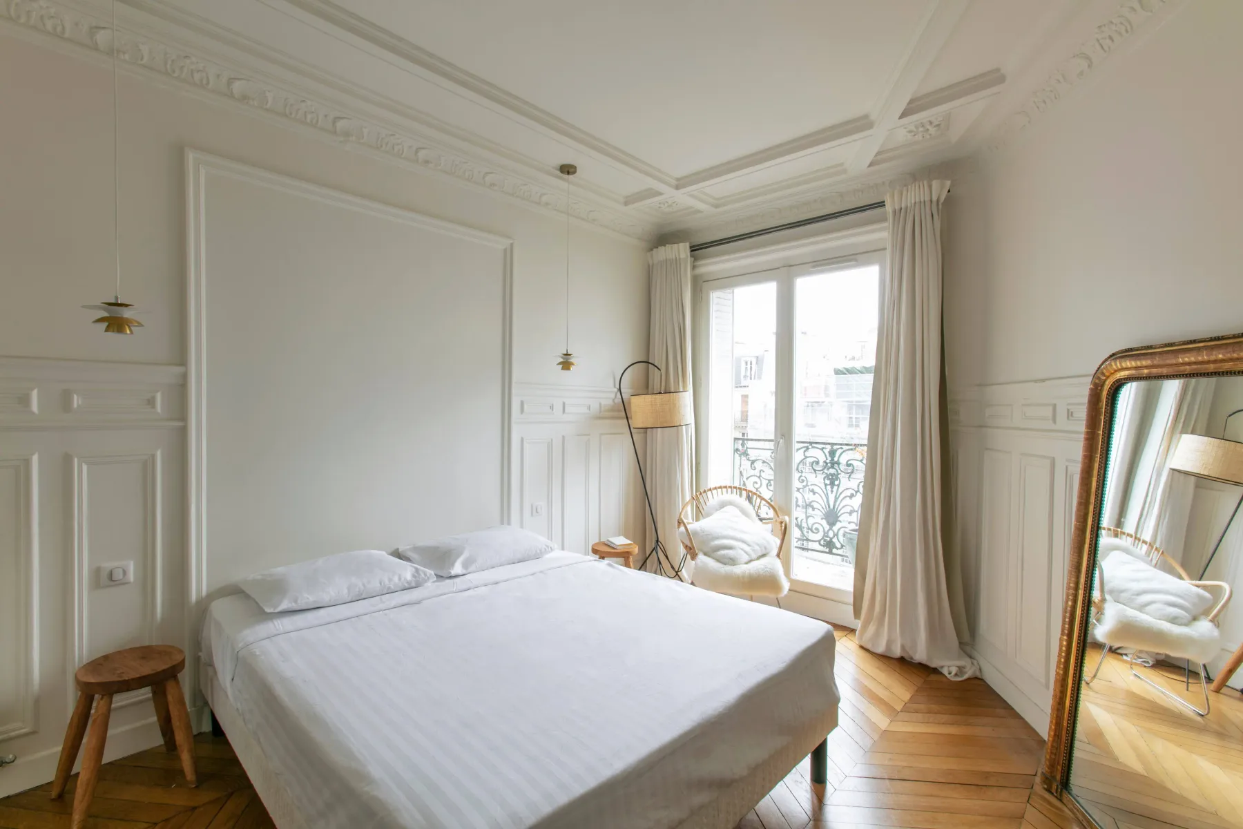 A bright bedroom with a bed, a window, and a large mirror.