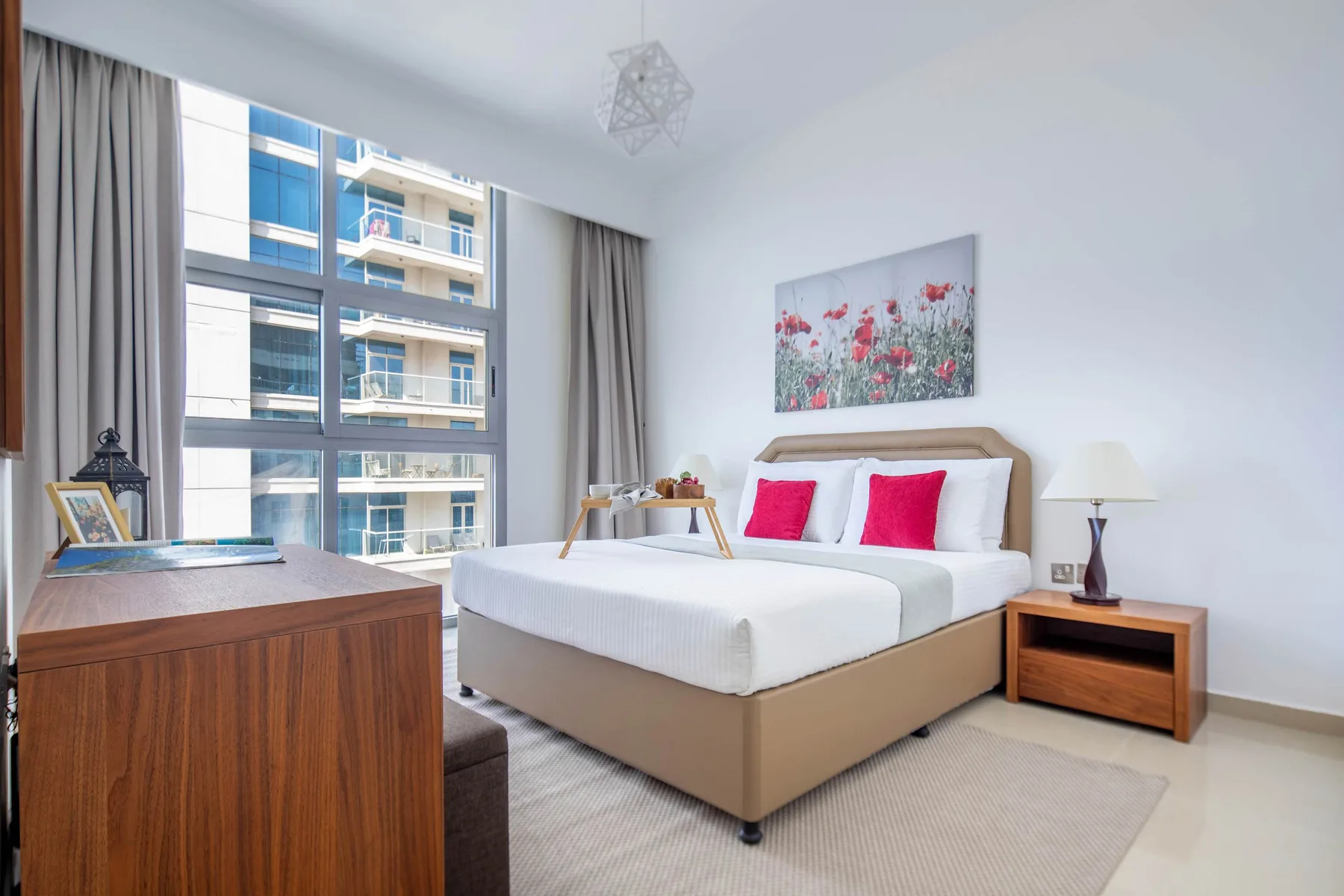 A bright bedroom with a bed, large windows, and a bedside table.