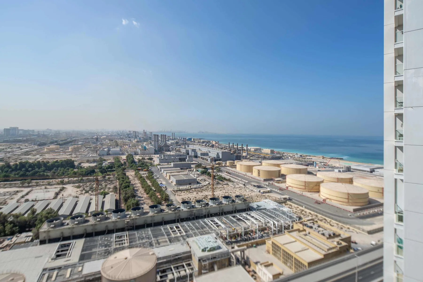 Coastal cityscape viewed from above, with industrial buildings and the sea beyond.