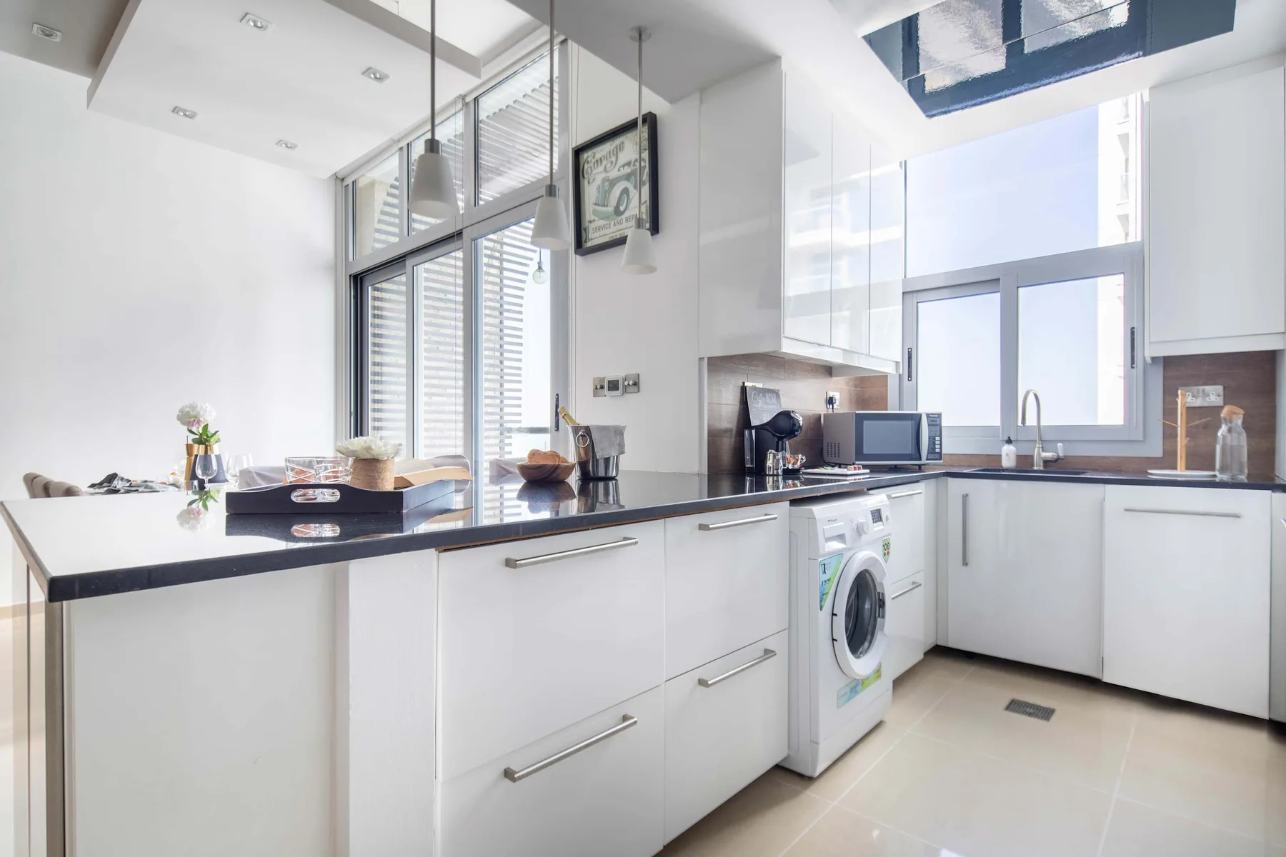 A bright modern kitchen with white cabinets, dark countertops, and a washing machine.