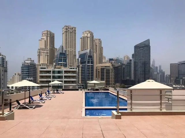 A rooftop pool deck with lounge seating and a city skyline in the background.