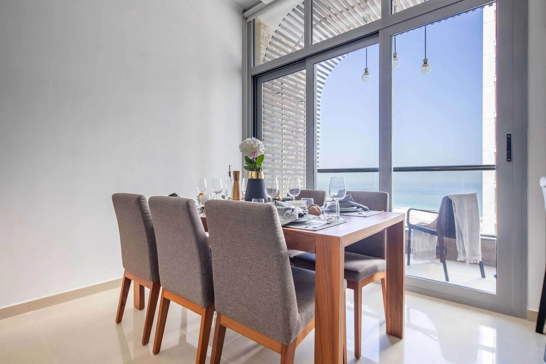 A dining area with a set table beside large windows overlooking the sea.